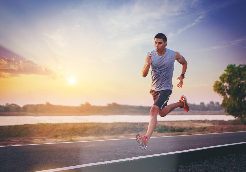 Silhouette of man running sprinting on road. Fit male fitness runner during outdoor workout with sunset background