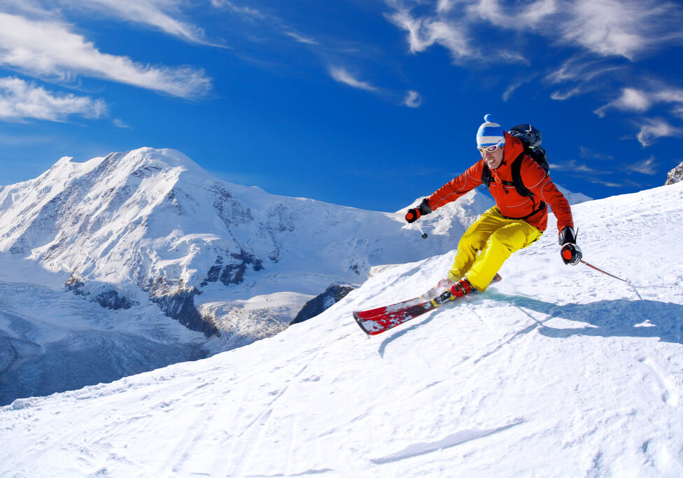 Skier skiing downhill in high mountains against blue sky